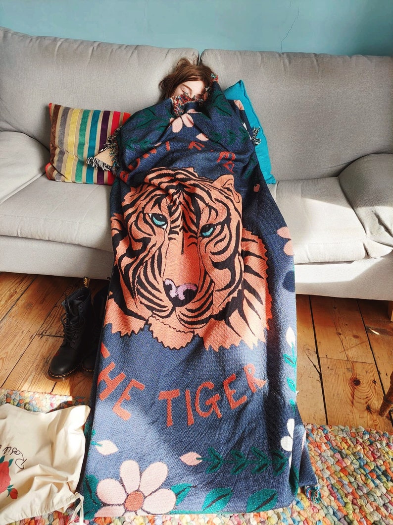 K&ouml;nnte beinhalten: Eine blaue und orangefarbene Wolldecke mit einem Tigergesicht und dem Aufdruck "Don't Be The Tiger". Die Decke ist aus weichem, flauschigem Material und hat ein Blumenmuster.