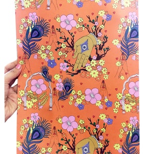 Peut inclure: Papier d'emballage orange avec un motif r&eacute;p&eacute;titif de fleurs roses, de plumes de paon et de mains dor&eacute;es en position de pri&egrave;re. Le fond est de couleur orange unie.