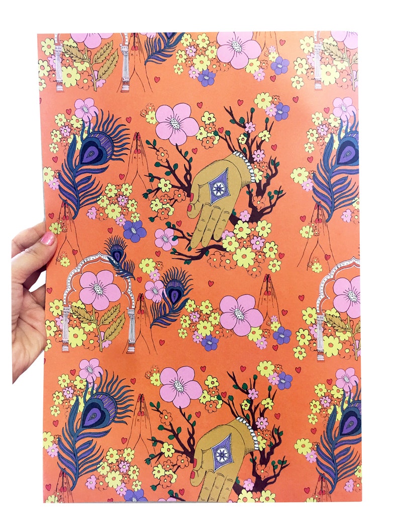 Peut inclure: Papier d'emballage orange avec un motif r&eacute;p&eacute;titif de fleurs roses, de plumes de paon et de mains dor&eacute;es en position de pri&egrave;re. Le fond est de couleur orange unie.