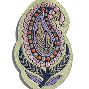 May include: A light green fabric patch with an embroidered paisley design. The paisley is in shades of pink, purple, orange, and gold. The patch has a decorative stitch around the edge.