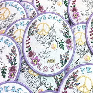 May include: A collection of round, purple-trimmed patches with a white background. Each patch features a stylised peace sign, a dove, and the words "Peace and Love". The patches are decorated with colourful flowers and leaves.