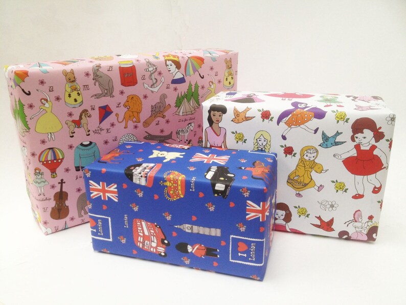 May include: Three gift boxes wrapped in colorful patterned paper. The top box is white with a floral pattern and features small illustrations of dolls and birds. The middle box is blue with a pattern of red hearts, British flags, and London landmarks. The bottom box is pink with a pattern of animals, toys, and other whimsical illustrations.
