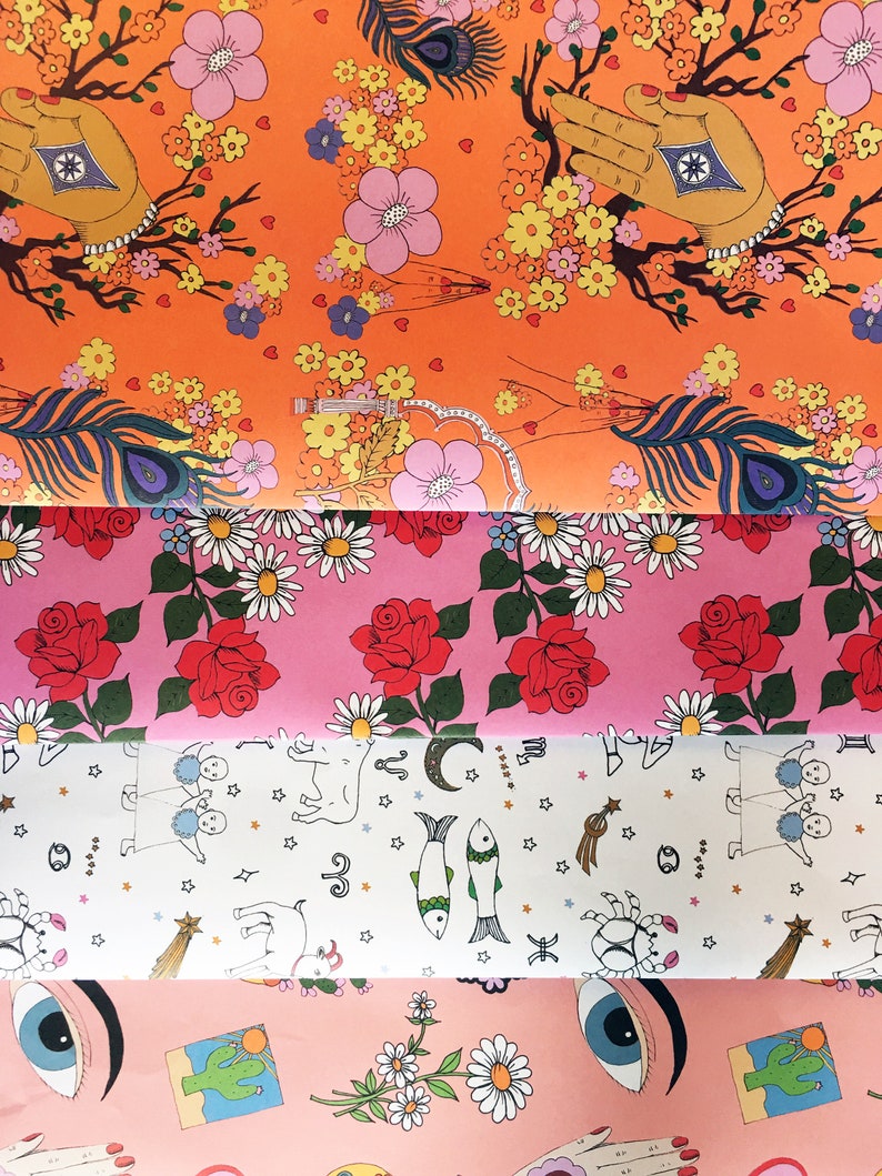 May include: Four different patterned wrapping papers. The top paper is orange with pink and yellow flowers, a peacock feather, and a hand with a star. The second paper is pink with red roses and white daisies. The third paper is white with black stars and zodiac symbols. The bottom paper is pink with a green cactus, a yellow sun, a white daisy, and a blue eye.