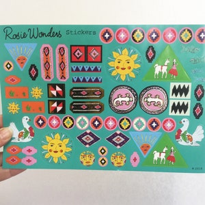 Pu&ograve; includere: Un foglio di adesivi colorati su sfondo turchese. Gli adesivi presentano vari disegni, tra cui soli, uccelli, motivi geometrici e lama. Il testo "Rosie Wonders Stickers" &egrave; stampato nella parte superiore del foglio.