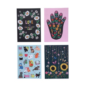 May include: Set of four greeting cards featuring colorful illustrations. One card has a black background with a wreath of white daisies and the text "Love is the answer". Another card has a pink background with a black hand with flowers and eyes. The third card has a blue background with a pattern of cats. The fourth card has a black background with a pattern of flowers and butterflies.