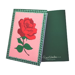 Puede incluir: Una libreta rosa con un borde verde y una ilustración de una rosa roja. La contraportada es verde con el texto "Rosie Wonders.co.uk" y "Booklet with lined pages".