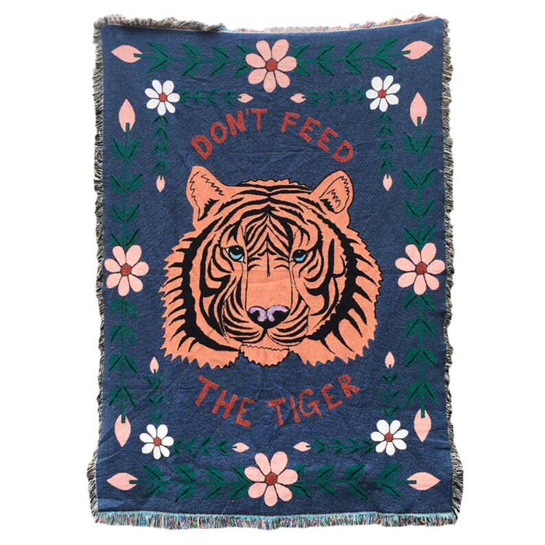 K&ouml;nnte beinhalten: Eine gewebte Wolldecke mit blauem Hintergrund und einem pinkfarbenen und orangen Tigergesicht in der Mitte. Der Text "Don't Feed The Tiger" ist in roten und wei&szlig;en Buchstaben &uuml;ber dem Tiger geschrieben. Die Decke ist mit gr&uuml;nen Ranken und pinkfarbenen und wei&szlig;en Blumen verziert.