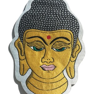 Puede incluir: Parche bordado de una cabeza de Buda dorada con un moño gris estampado, ojos verdes y un punto rojo en la frente.
