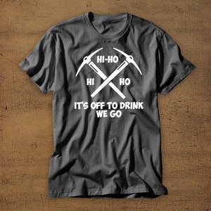 Puede incluir: Una camiseta gris oscuro con un gr&aacute;fico blanco de dos picos cruzados y el texto "Hi-Ho Hi Ho It's Off To Drink We Go".