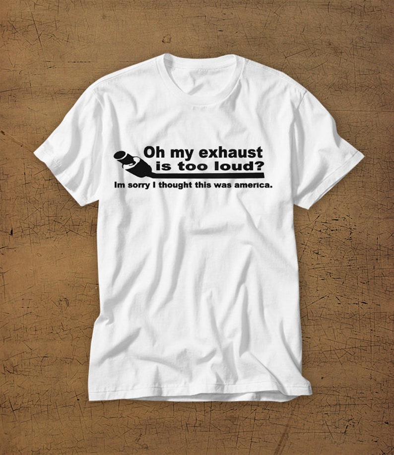 May include: White t-shirt with a black graphic of a car exhaust pipe and the text "Oh my exhaust is too loud? Im sorry I thought this was america."