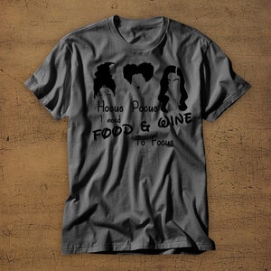 May include: A dark gray t-shirt with a black graphic of three witches from the movie Hocus Pocus. The text reads "Hocus Pocus I need Food & Wine To Focus".