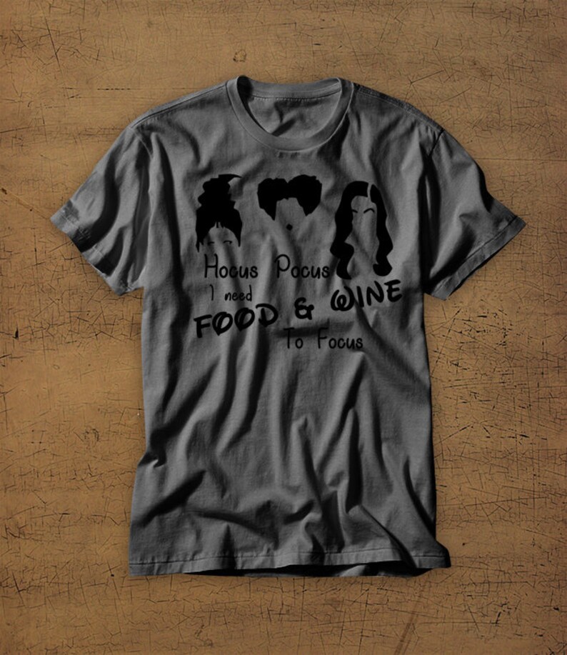 May include: A dark gray t-shirt with a black graphic of three witches from the movie Hocus Pocus. The text reads "Hocus Pocus I need Food & Wine To Focus".