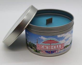 Könnte beinhalten: Eine silberne Dose mit einer blauen Wachsoberfläche und einem Etikett mit der Aufschrift "Beach Club Resort". Das Etikett zeigt einen rot-weiß gestreiften Sonnenschirm und einen blauen Himmel mit weißen Wolken.