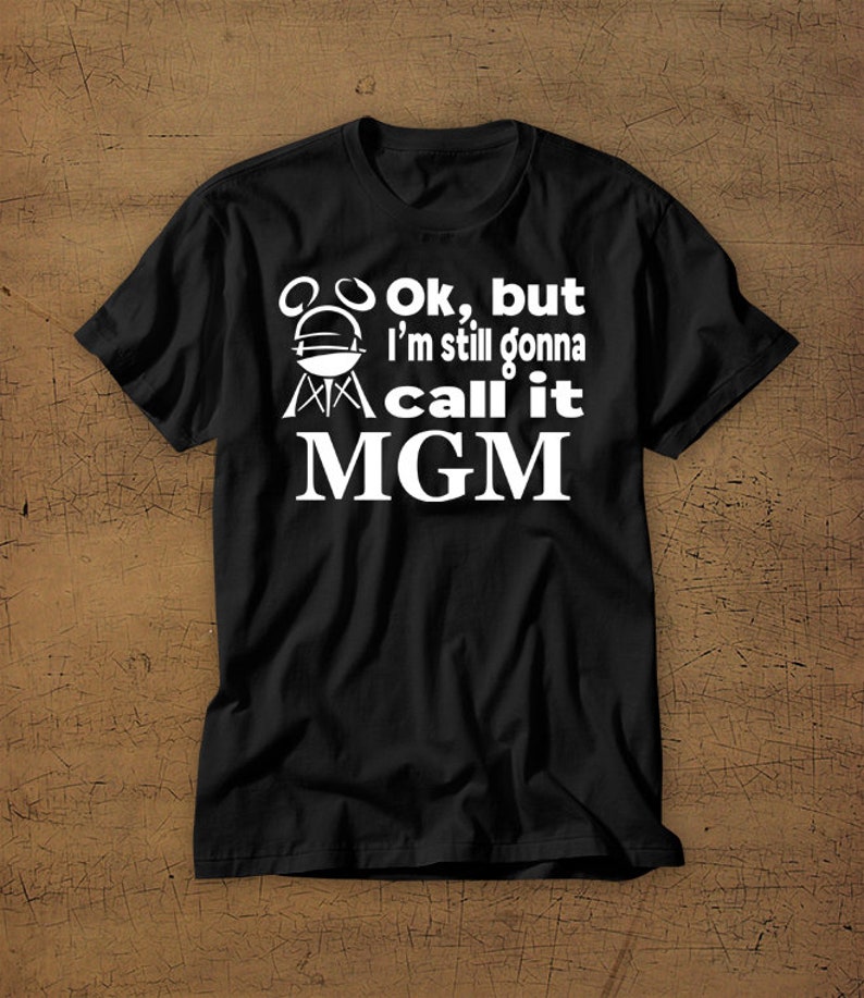 May include: Black t-shirt with white text that reads "Ok, but I'm still gonna call it MGM" with a grill graphic.