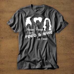 May include: A dark gray t-shirt with a white graphic of the Sanderson sisters from the movie Hocus Pocus. The text reads "Hocus Pocus I need Food & Wine To Focus".