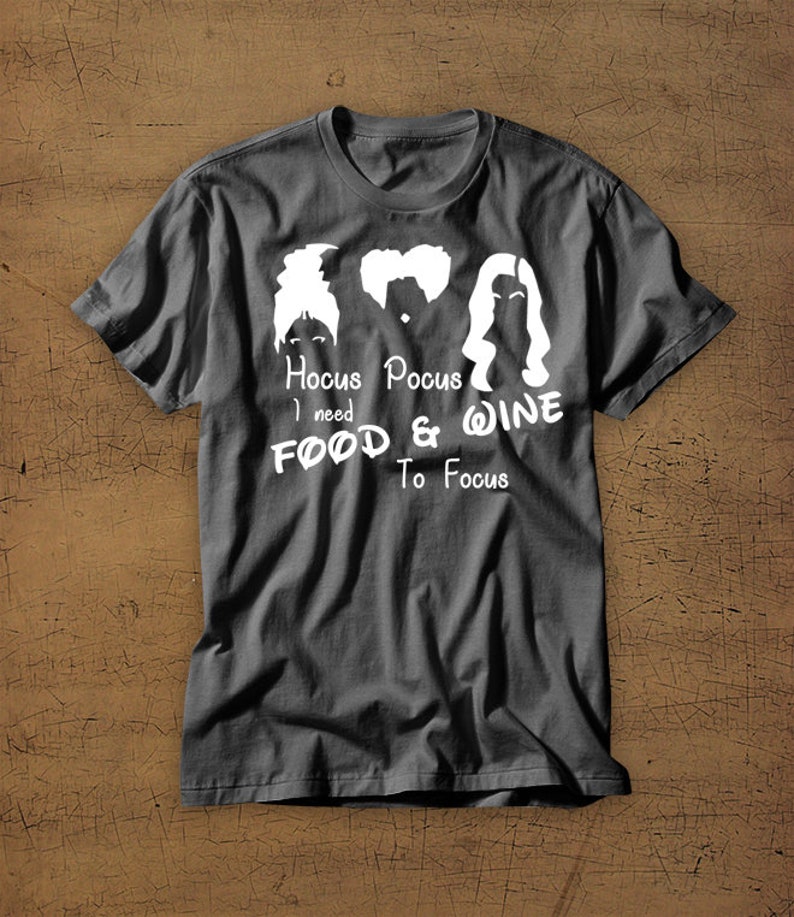 May include: A dark gray t-shirt with a white graphic of the Sanderson sisters from the movie Hocus Pocus. The text reads "Hocus Pocus I need Food & Wine To Focus".