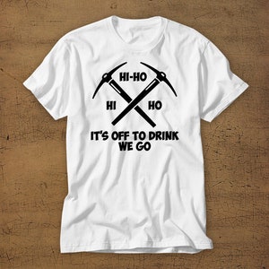 Puede incluir: Camiseta blanca con un gr&aacute;fico negro de dos picos cruzados y el texto "Hi-Ho Hi Ho It's Off To Drink We Go".