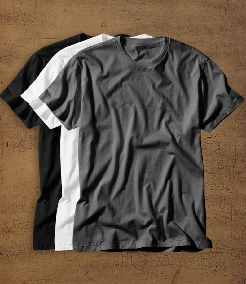 May include: Three plain t-shirts in black, white, and gray. The shirts are folded and stacked on top of each other.