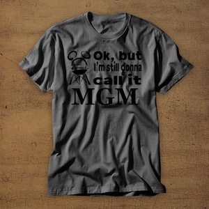 May include: A dark gray t-shirt with a black graphic that says "Ok, but I'm still gonna call it MGM" with a grill icon.