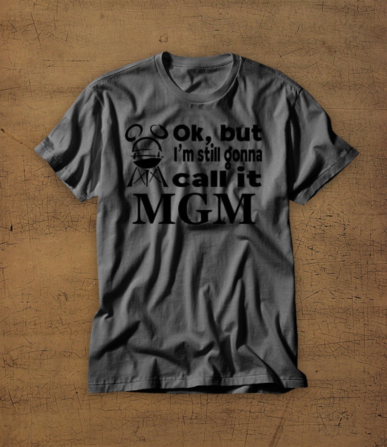 May include: A dark gray t-shirt with a black graphic that says "Ok, but I'm still gonna call it MGM" with a grill icon.