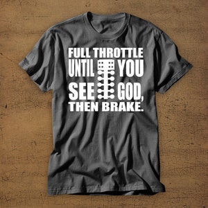 May include: A dark grey t-shirt with a white graphic that reads "Full Throttle Until You See God, Then Brake." The graphic also includes a white silhouette of a drag racing Christmas tree.