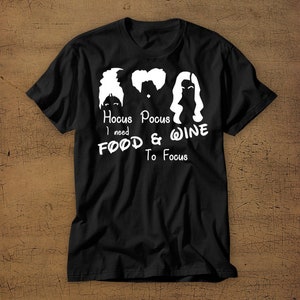 May include: Black t-shirt with a white graphic of the Sanderson sisters from the movie Hocus Pocus. The text reads "Hocus Pocus I need Food & Wine To Focus".