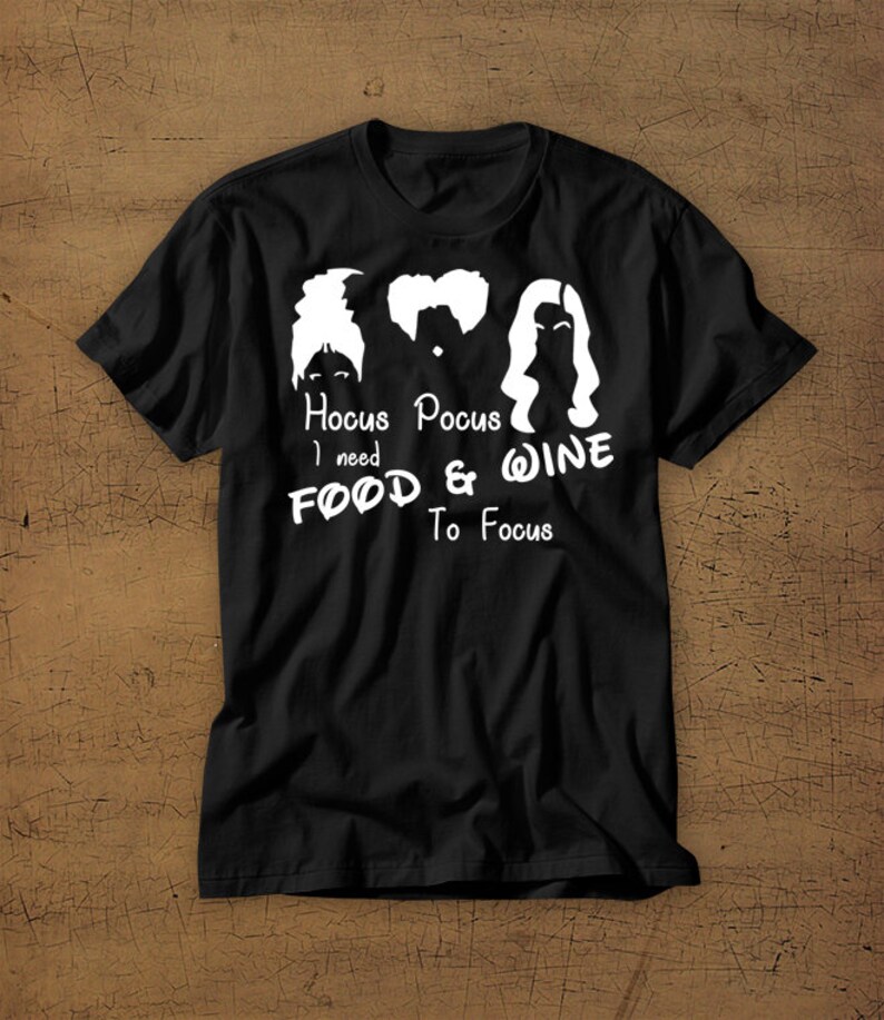 May include: Black t-shirt with a white graphic of the Sanderson sisters from the movie Hocus Pocus. The text reads "Hocus Pocus I need Food & Wine To Focus".