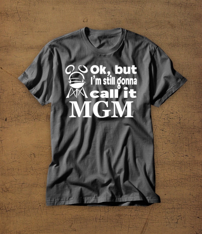 May include: A dark gray t-shirt with a white graphic that says "Ok, but I'm still gonna call it MGM" with a grill icon.