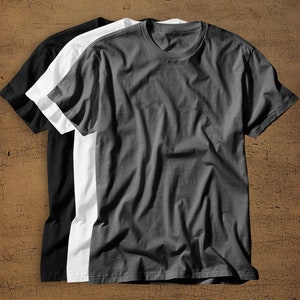 May include: Three plain t-shirts in black, white, and gray. The shirts are folded and stacked on top of each other.