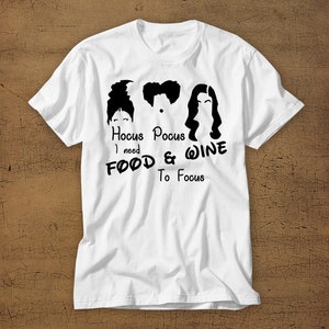May include: White t-shirt with a black graphic of the Sanderson sisters from the movie Hocus Pocus. The text reads "Hocus Pocus I need FOOD & WINE To Focus".
