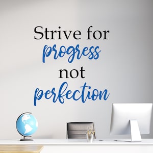 Puede incluir: Una calcomanía de pared motivacional con el texto "Strive for progress not perfection" en letras negras y azules. La calcomanía se muestra en una pared blanca en un entorno de aula.