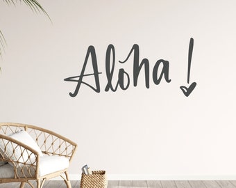 Pode incluir: Uma cadeira de vime branca com uma almofada branca está em frente a uma parede branca com a palavra "Aloha!" escrita em caligrafia preta.