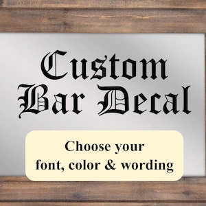 Puede incluir: Un letrero enmarcado con el texto "Custom Bar Decal" en una fuente negra de estilo inglés antiguo. El letrero tiene un fondo crema con el texto "Choose your font, color & wording" en negro.