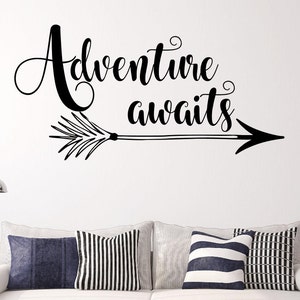 May include: Black and white wall decal with the text "Adventure awaits" and an arrow pointing to the right. The decal is on a white wall above a white couch with black and white striped pillows.