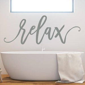May include: A white bathtub with a grey towel draped over the edge. The word "relax" is written in grey cursive script on the wall above the bathtub.