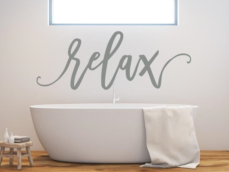 May include: A white bathtub with a grey towel draped over the edge. The word "relax" is written in grey cursive script on the wall above the bathtub.