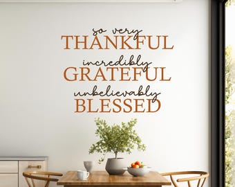 May include: A wall decal with the words "so very THANKFUL incredibly GRATEFUL unbelievably BLESSED" in brown and black lettering. A small plant in a gray pot sits on a wooden table with two chairs.