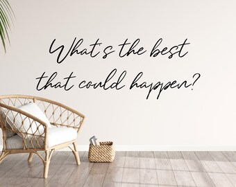 May include: A white wall with the text "What's the best that could happen?" written in black cursive. A wicker chair with a white cushion sits in front of the wall. A wicker basket with a few items inside sits on the wooden floor.