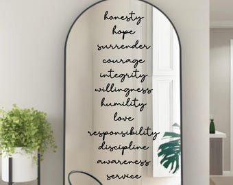 May include: An arched mirror with a black frame displays a list of words in elegant script: honesty, hope, surrender, courage, integrity, willingness, humility, love, responsibility, discipline, awareness, and service. A potted plant is visible on the left.