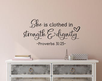 May include: A wall decal with the quote "She is clothed in strength & dignity - Proverbs 31:25" in elegant black script. The quote is above a white dresser with decorative items.