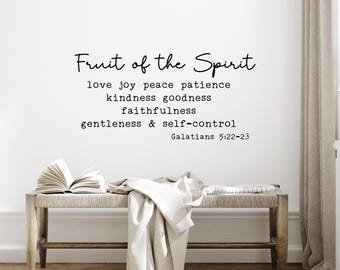 May include: A wall art piece with the text "Fruit of the Spirit" and related virtues. Below, a bench with a book and draped fabric. The text includes "love joy peace patience kindness goodness faithfulness gentleness & self-control Galatians 5:22-23".
