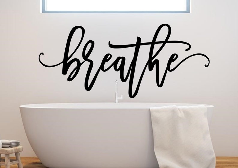Puede incluir: Adhesivo de pared negro con la palabra "breathe" en escritura cursiva sobre una ba&ntilde;era blanca. Una toalla blanca cuelga del borde de la ba&ntilde;era. El ba&ntilde;o tiene un dise&ntilde;o minimalista.