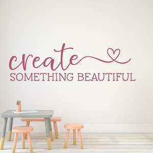 Pu&ograve; includere: Adesivo da parete rosa con il testo "create something beautiful" e un simbolo di cuore.