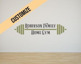 May include: Wall decal featuring the text "Robinson Family Home Gym" in a stylized font, with a barbell graphic. The word "Customize" is on a diagonal yellow banner. The decal is on a white wall above a wood floor.