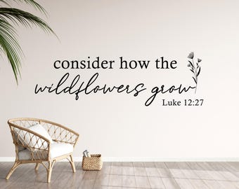 May include: A white wall with a black and white quote that reads "consider how the wildflowers grow Luke 12:27". A potted plant is in the corner of the image and a wicker chair is in the foreground.