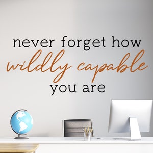 Op de afbeelding: Een motiverende quote op een witte muur die luidt "vergeet nooit hoe ongelooflijk bekwaam je bent". De quote is in zwarte en bruine letters. Op de achtergrond zijn een globe, een computerscherm en een bureau met kantoorbenodigdheden te zien.