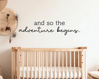 May include: A white wall with the text "and so the adventure begins..." written in black. A wooden crib with a white mattress is in the foreground.