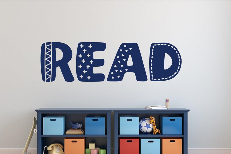 May include: Blue and white wall decal with the word "READ" in a playful, patterned font. The decal is on a white wall above a blue bookshelf with colourful storage bins.
