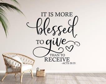 May include: A wall decal with the phrase "IT IS MORE BLESSED TO GIVE THAN TO RECEIVE" in black script. A heart symbol is included. A wicker chair and small basket are in the foreground.