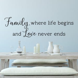 Könnte beinhalten: Eine weiße Wand mit schwarzem Text, der "Family, where life begins and Love never ends" lautet. Im Vordergrund steht ein Holztisch mit weißen Tellern und einer weißen Kanne.